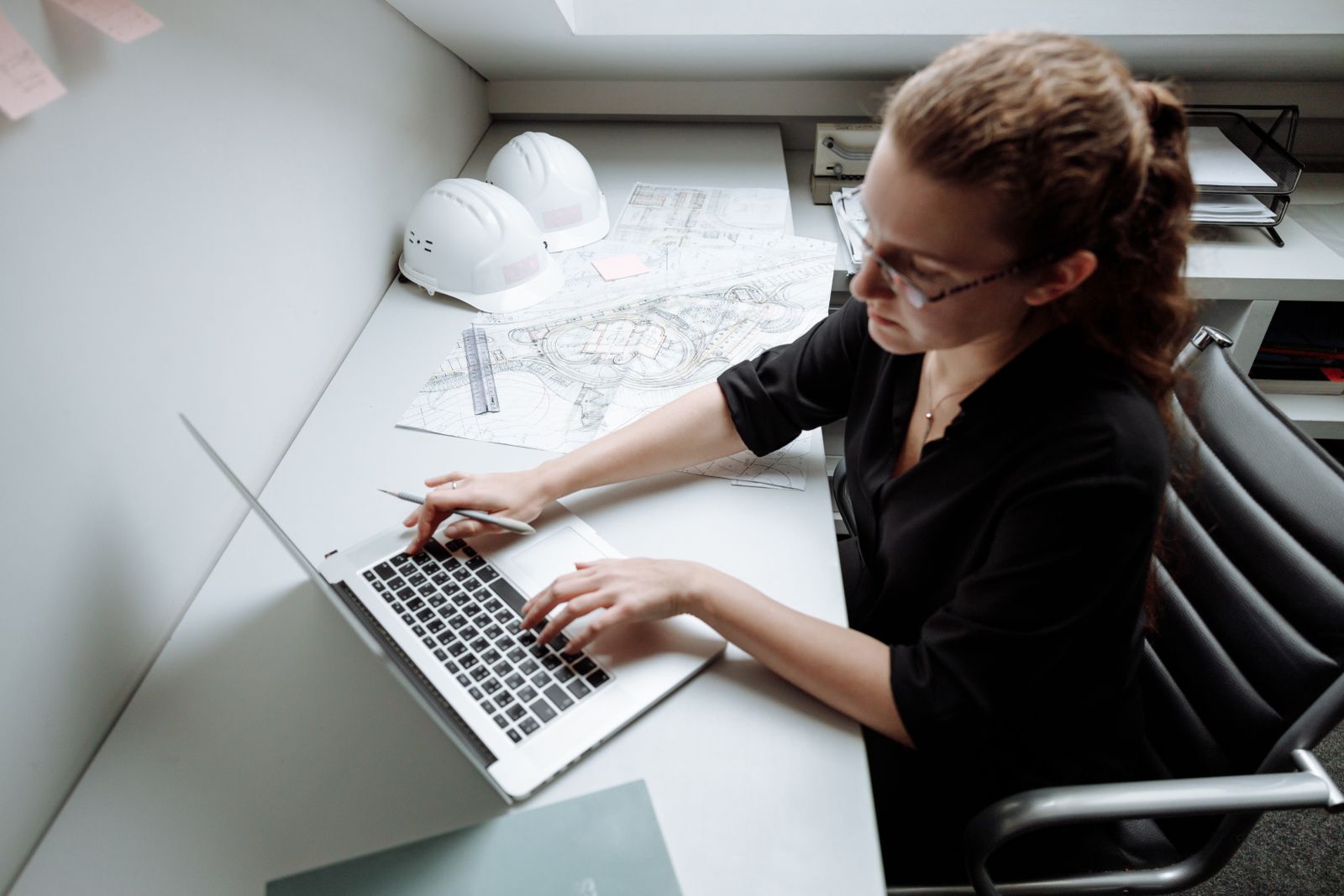 Camille Faure à son bureau, travaillant sur des plans, casque de chantier posé à côté.