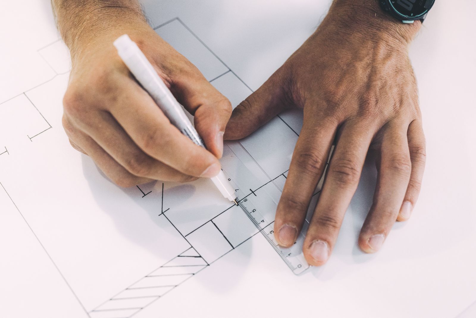 Mains traçant un plan à la règle et au stylo.