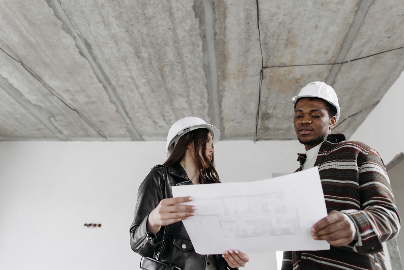 Deux architectes en casques examinent des plans dans un bâtiment en travaux.