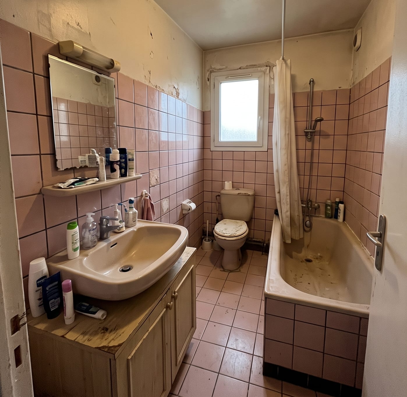 Salle de bain vétuste avant travaux : carrelage rose, baignoire et faïence abîmée.