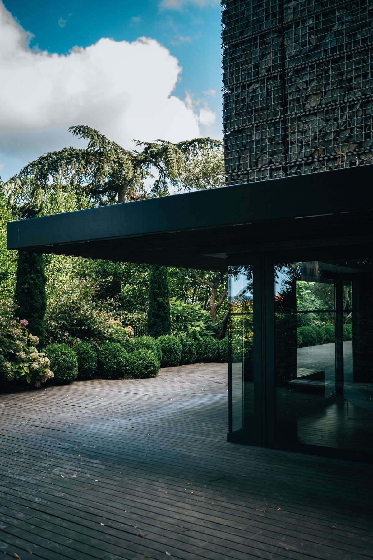 Façade contemporaine entourée d’un jardin planté et d’une terrasse en bois.