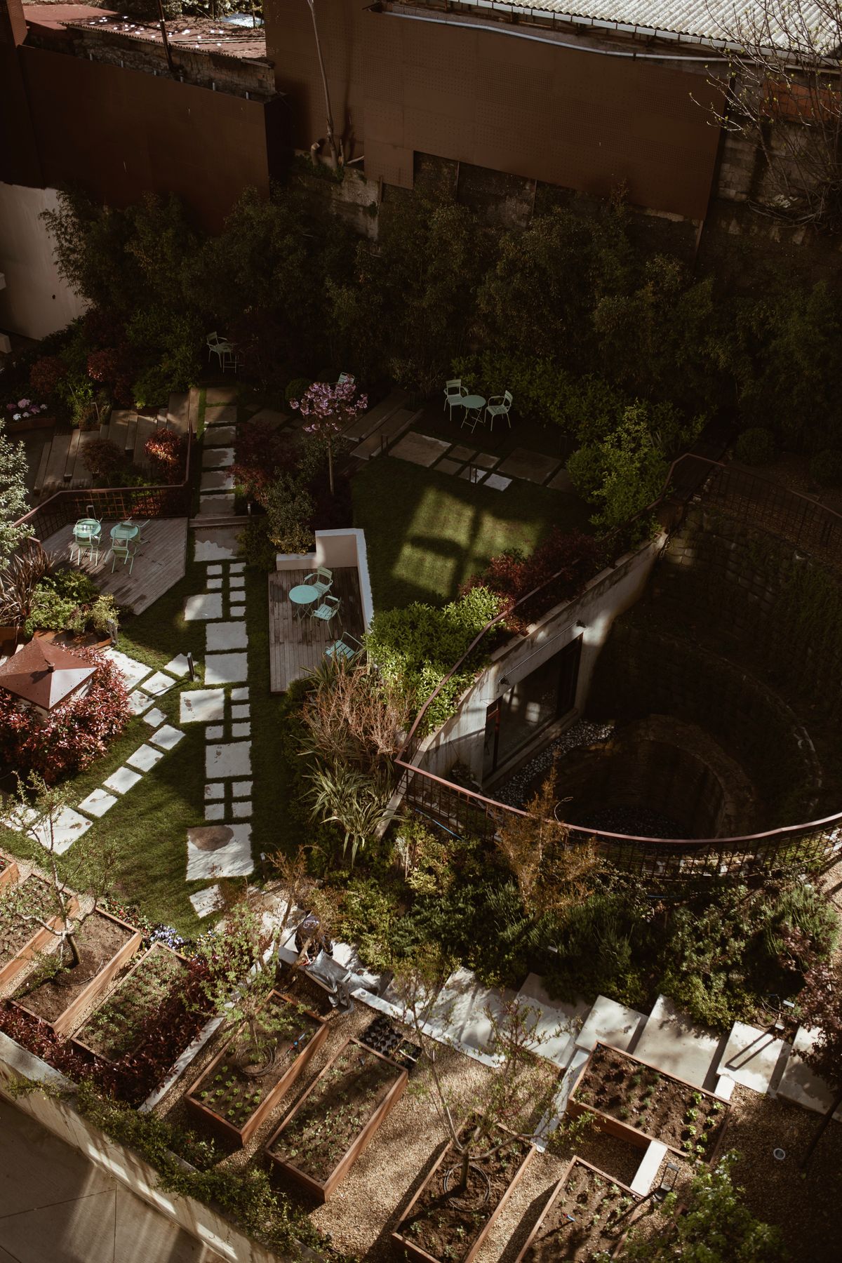Jardin de ville vu d’en haut, avec terrasse, chemins et coins de verdure.