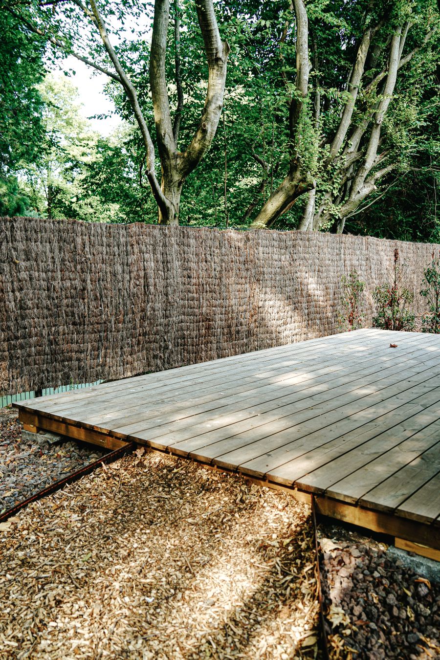 Terrasse en bois entourée d’arbres, avec sa clôture.
