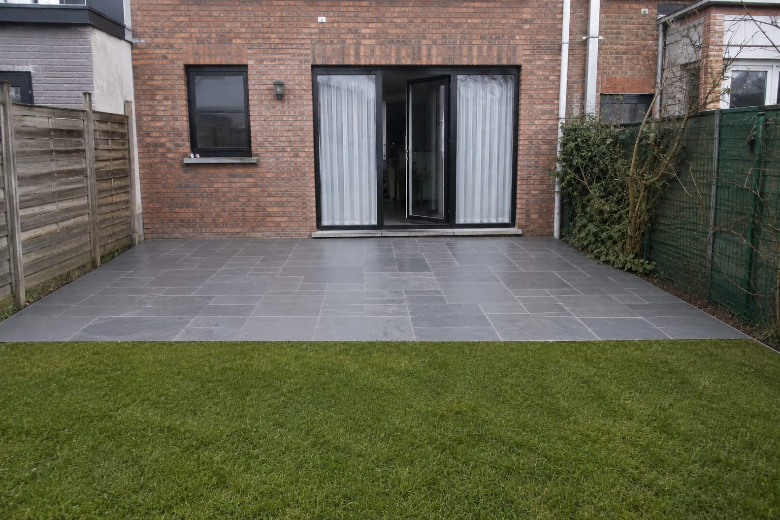 Même arrière de maison après travaux : terrasse en pierre bleue posée à joints serrés, bordure droite et pelouse reprise.