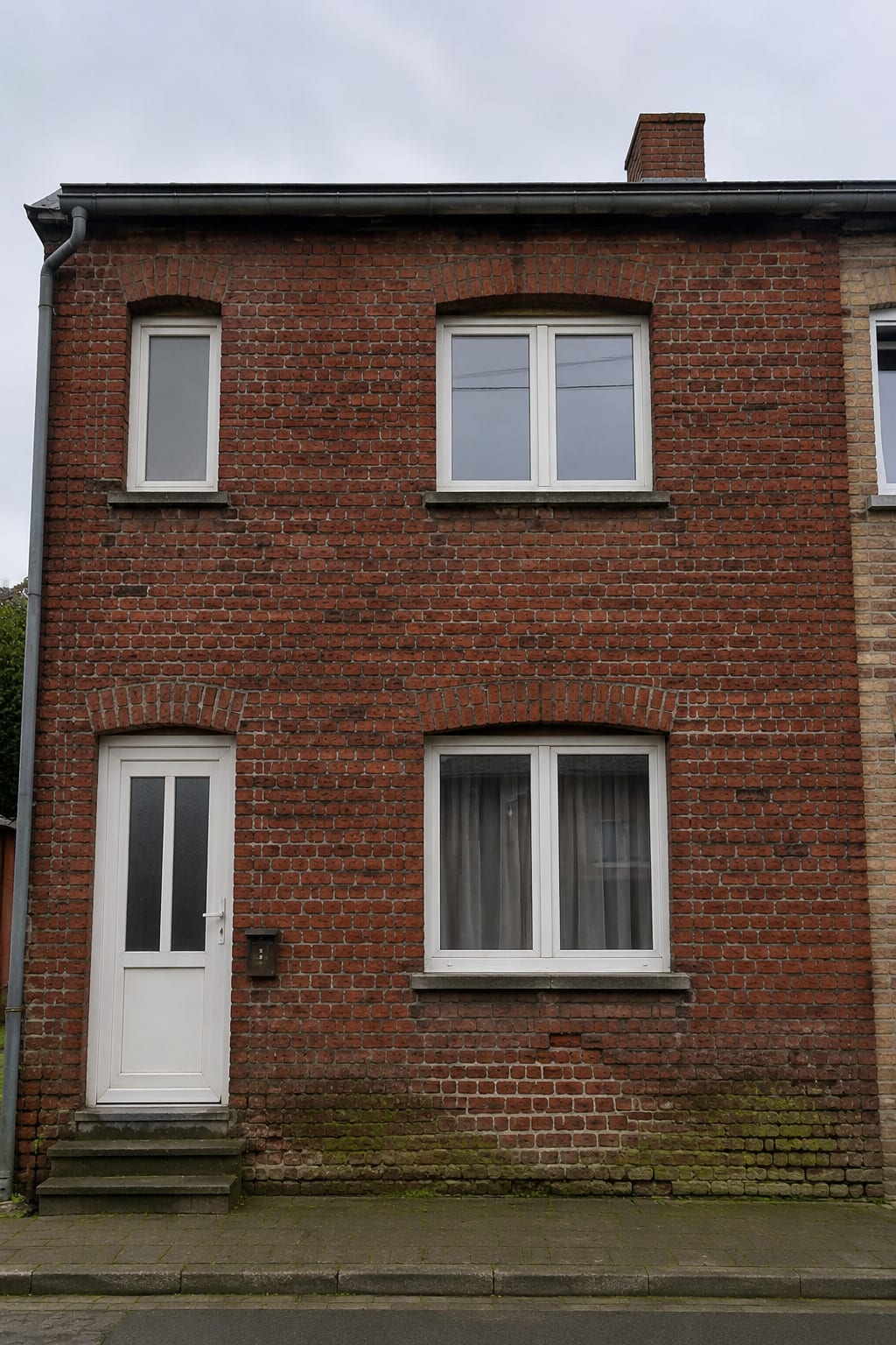 Façade de maison en briques avant travaux : joints creusés et noircis, mousses vertes et briques épaufrées par endroits.
