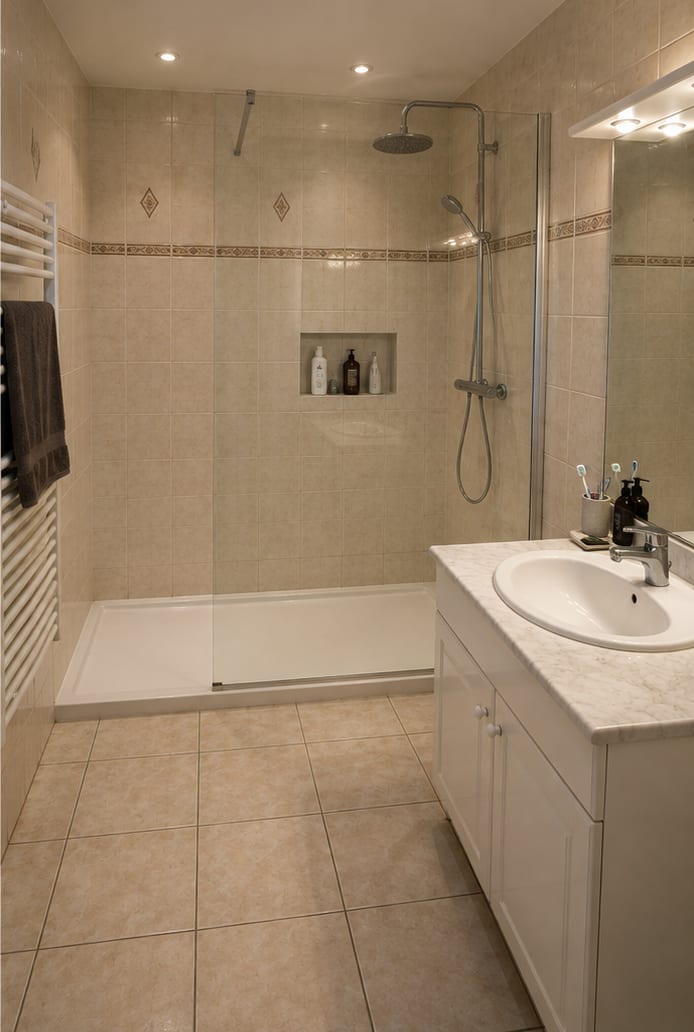 Même salle de bain après travaux : douche avec receveur extra-plat, paroi vitrée, colonne de douche et niche de rangement carrelée.