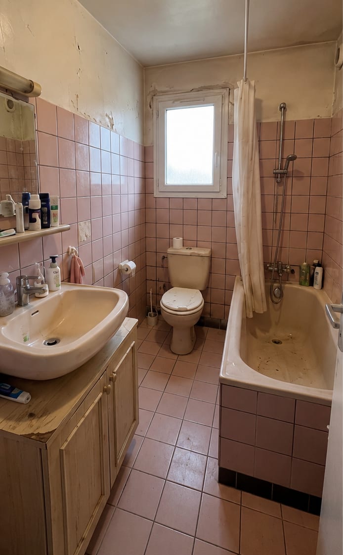 Salle de bain avant travaux : meuble vasque en bois vieilli, lavabo et baignoire entartrés, peinture écaillée au-dessus de la faïence rose.
