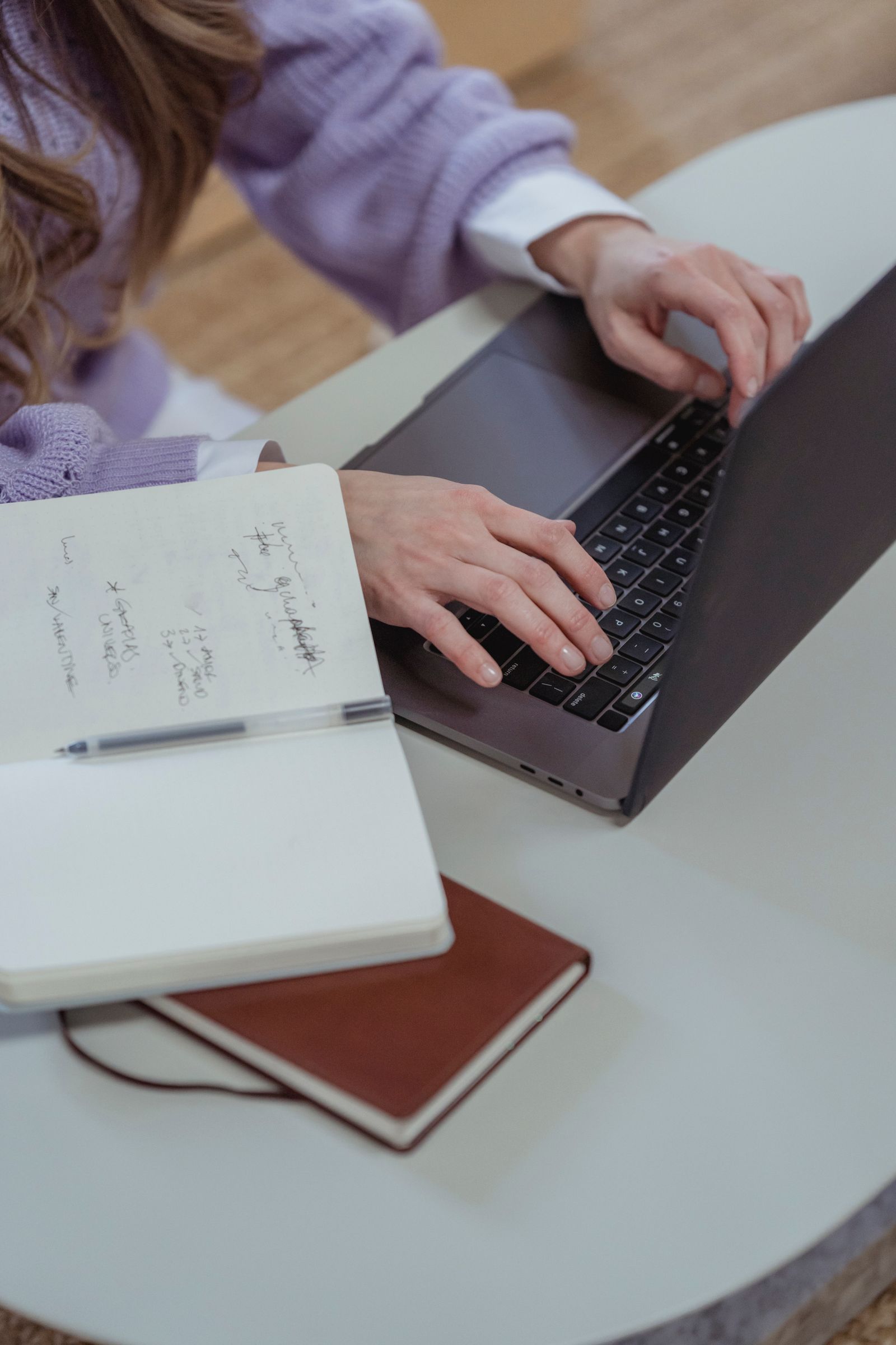 Femme concentrée qui écrit sur son ordinateur, carnet à côté.